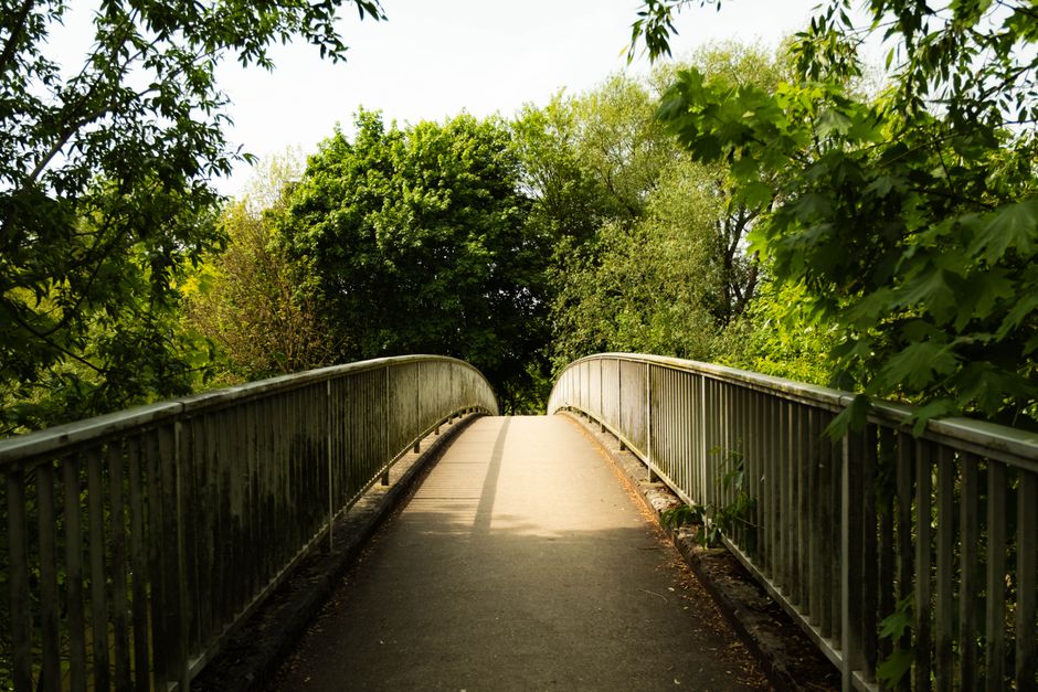 An aerial black-and-white photograph of Upminster Bridge showing the River Ingrebourne flowing beneath a white stone arch bridge. The river is bordered by lush, leafy trees on both sides, with some tr